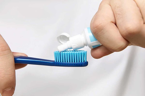A close-up of a person squeezing toothpaste onto a blue toothbrush, focusing on the hands and toothbrush bristles.