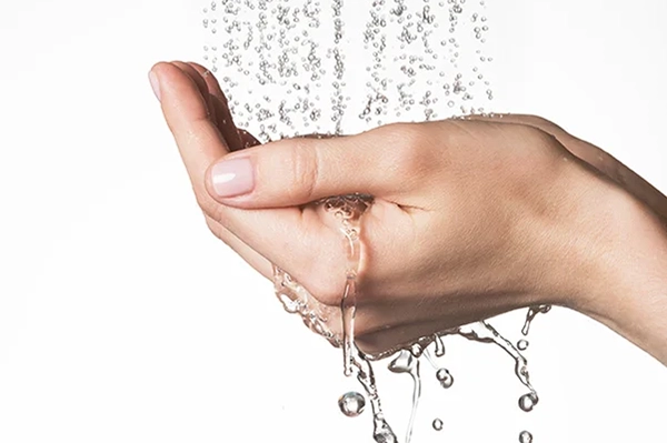 A close-up of hands held together under a stream of running water, with droplets splashing and flowing through the fingers.